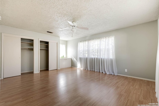 unfurnished bedroom with hardwood / wood-style floors, ceiling fan, a textured ceiling, and two closets