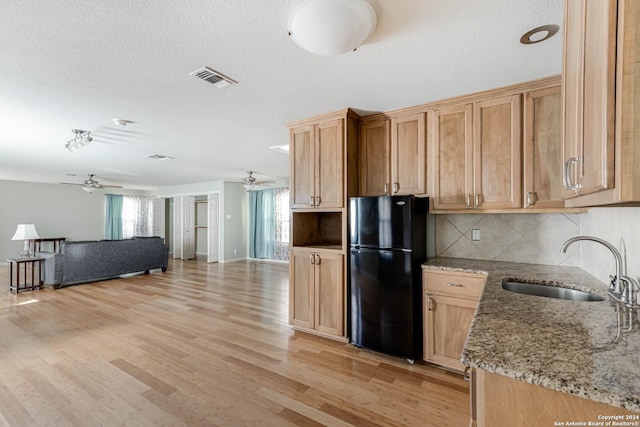 kitchen featuring backsplash, light stone counters, black fridge, sink, and light hardwood / wood-style flooring