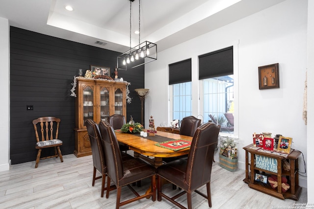 dining space with light wood-type flooring, wooden walls, and a tray ceiling