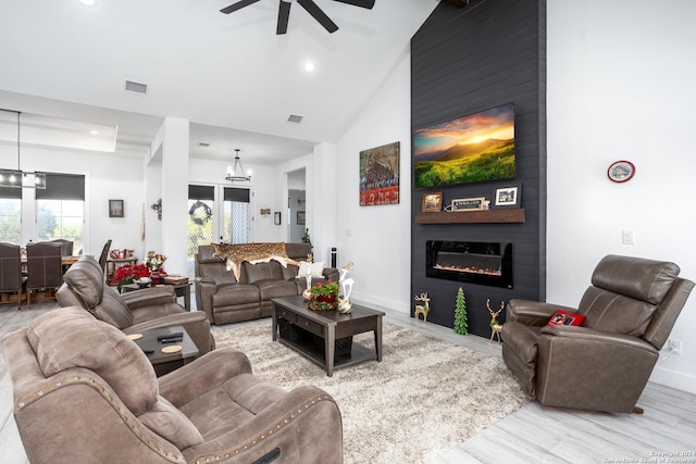 living room with high vaulted ceiling, french doors, ceiling fan with notable chandelier, light wood-type flooring, and a large fireplace