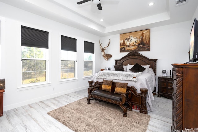 bedroom with ceiling fan, light wood-type flooring, and a tray ceiling