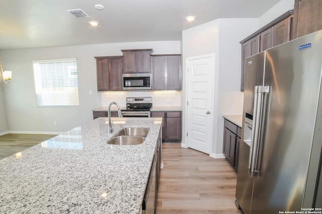 kitchen with sink, light wood-type flooring, tasteful backsplash, light stone counters, and stainless steel appliances