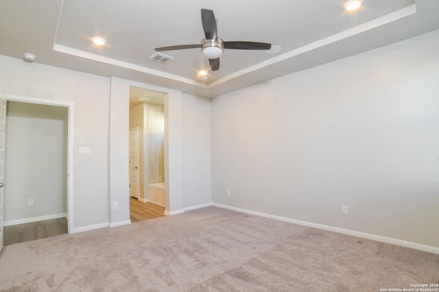 unfurnished bedroom with ceiling fan, a raised ceiling, light colored carpet, and ensuite bath