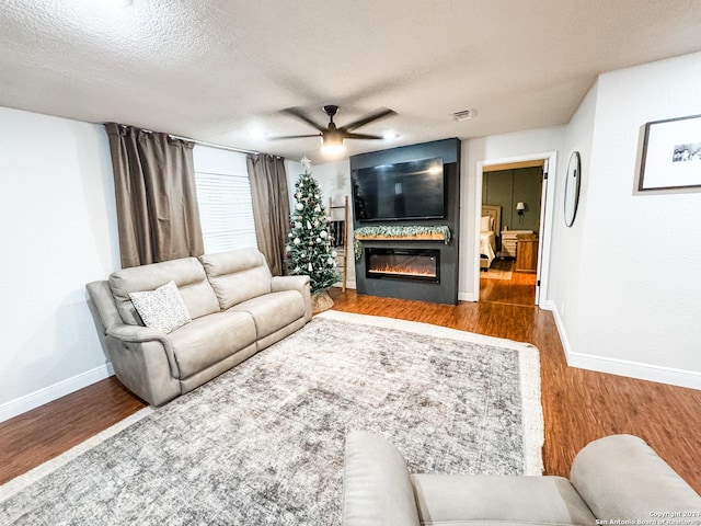 living room featuring a fireplace, a textured ceiling, hardwood / wood-style flooring, and ceiling fan