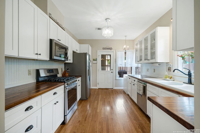 kitchen with butcher block countertops, white cabinetry, pendant lighting, and appliances with stainless steel finishes