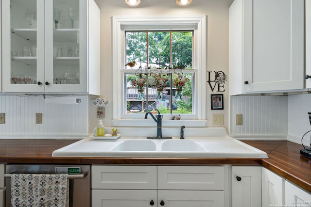 kitchen featuring dishwasher, butcher block countertops, white cabinetry, and sink