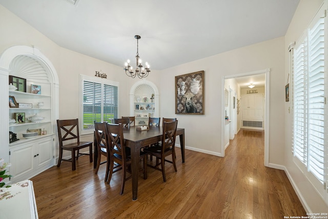 dining room with hardwood / wood-style floors, built in shelves, and an inviting chandelier