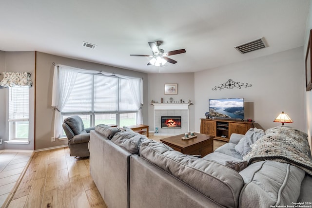 living room featuring a tile fireplace, light wood-type flooring, and ceiling fan