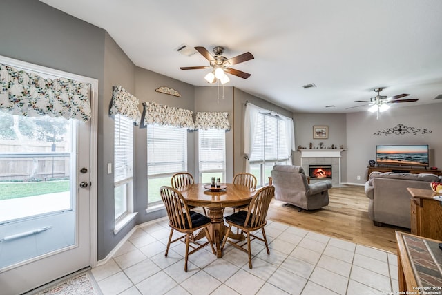 dining area featuring a tile fireplace, light tile patterned floors, and ceiling fan