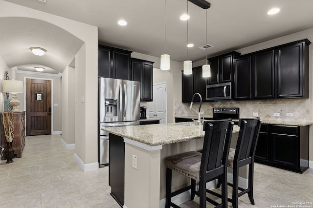 kitchen with a center island with sink, decorative backsplash, light stone countertops, appliances with stainless steel finishes, and decorative light fixtures