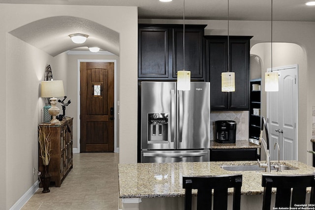 kitchen with decorative backsplash, light stone counters, sink, stainless steel fridge with ice dispenser, and hanging light fixtures