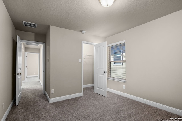 unfurnished bedroom featuring carpet flooring, a spacious closet, a textured ceiling, and a closet