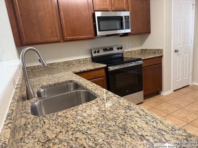 kitchen featuring light stone countertops, appliances with stainless steel finishes, light tile patterned floors, and sink