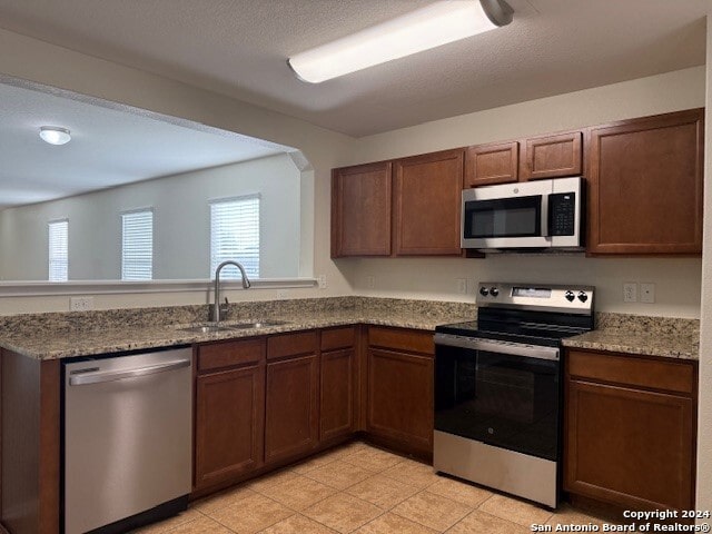 kitchen featuring kitchen peninsula, light stone countertops, sink, and appliances with stainless steel finishes