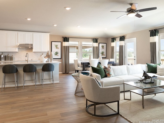 living room with light wood-type flooring, ceiling fan, and sink