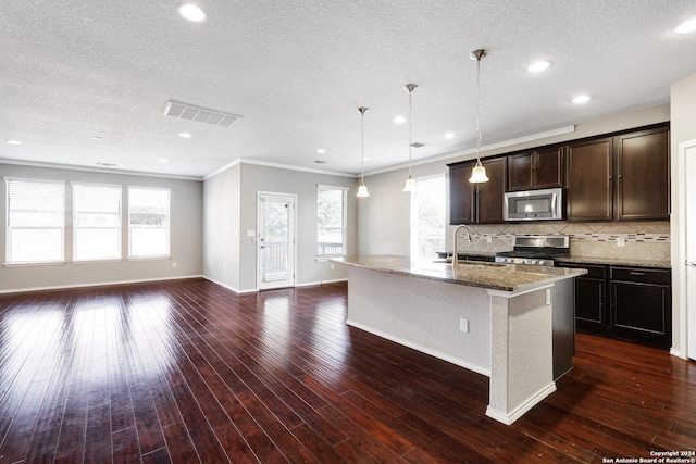 kitchen featuring stone counters, crown molding, an island with sink, decorative light fixtures, and appliances with stainless steel finishes