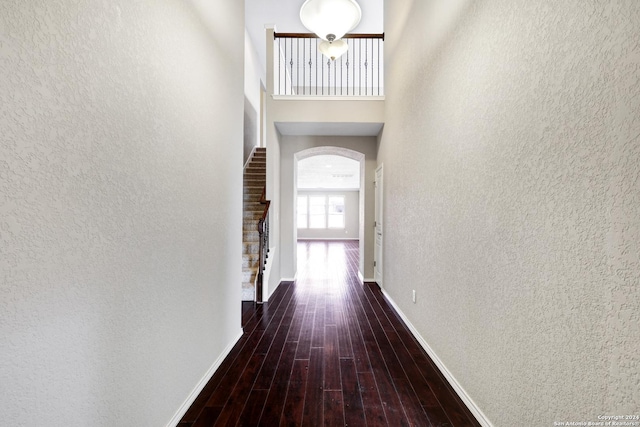 corridor with dark hardwood / wood-style flooring and a towering ceiling