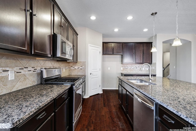 kitchen with appliances with stainless steel finishes, dark hardwood / wood-style flooring, light stone counters, sink, and pendant lighting