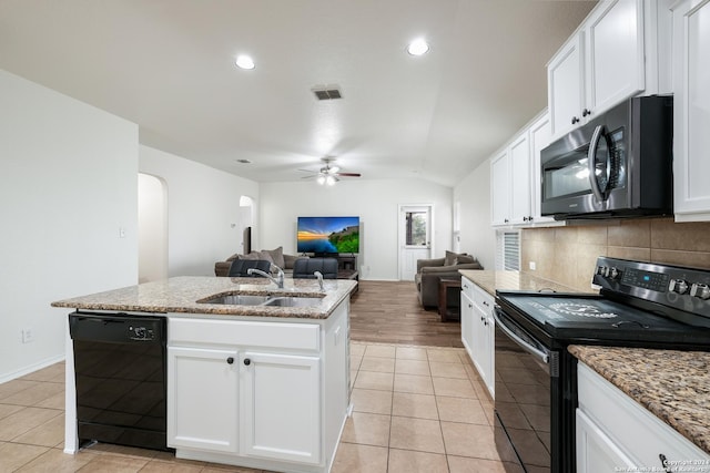 kitchen featuring sink, light stone counters, a kitchen island with sink, white cabinets, and black appliances