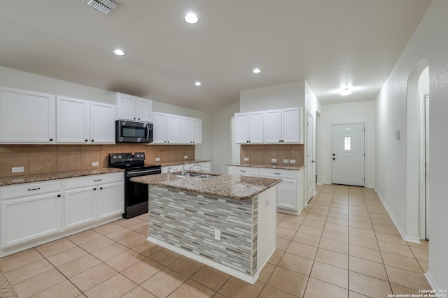 kitchen featuring light stone countertops, electric range, a center island with sink, and white cabinets