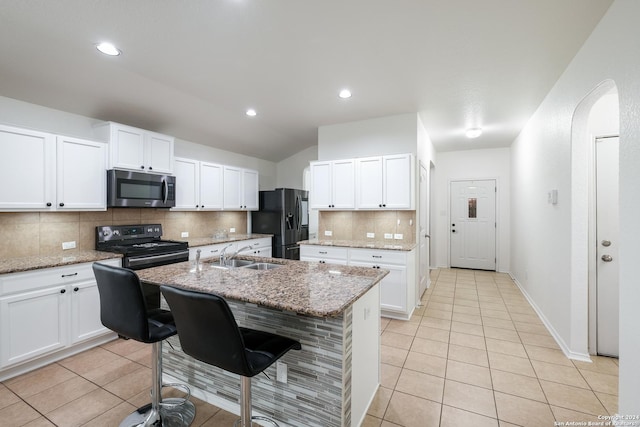 kitchen with sink, light stone counters, black electric range oven, refrigerator with ice dispenser, and a kitchen island with sink