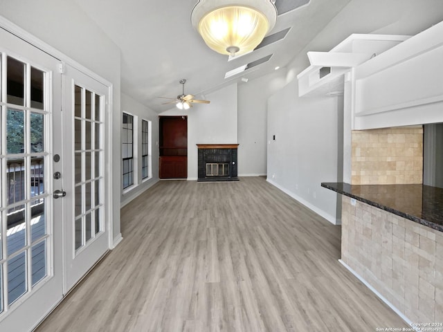 unfurnished living room featuring french doors, vaulted ceiling, ceiling fan, a fireplace, and light hardwood / wood-style floors