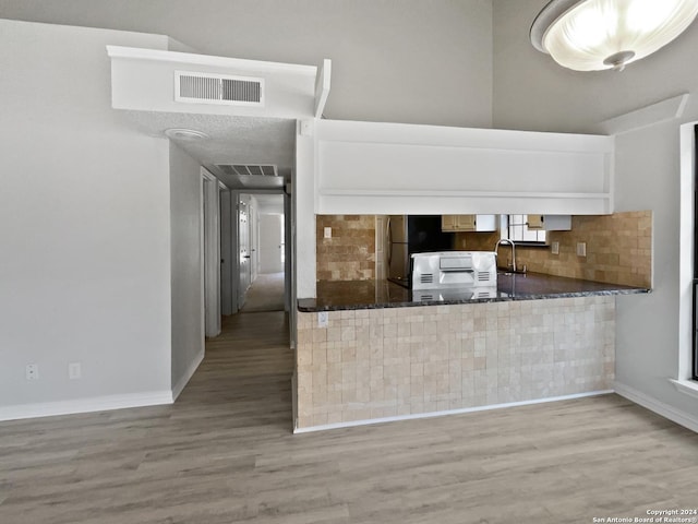 kitchen with kitchen peninsula, tasteful backsplash, light hardwood / wood-style flooring, and sink