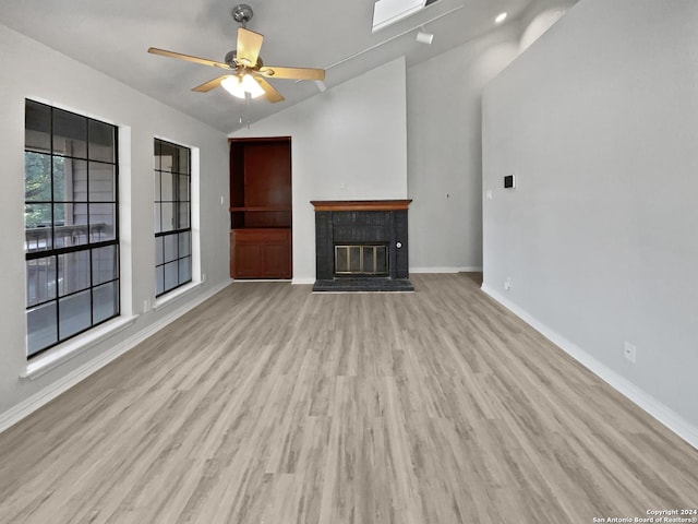 unfurnished living room with ceiling fan, lofted ceiling, light hardwood / wood-style flooring, and a tiled fireplace