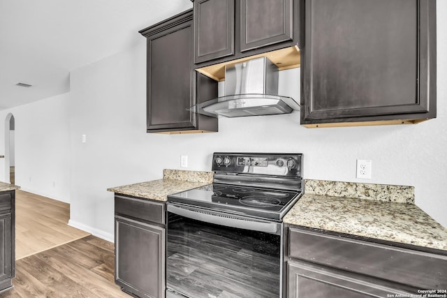 kitchen featuring light stone countertops, light hardwood / wood-style flooring, black electric range oven, and exhaust hood