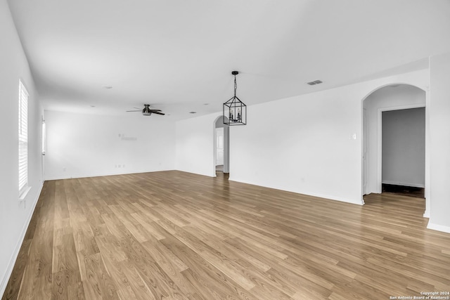 unfurnished living room featuring plenty of natural light, light hardwood / wood-style flooring, and ceiling fan with notable chandelier