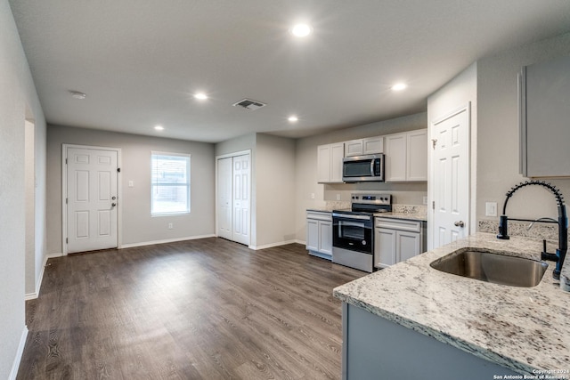 kitchen featuring white cabinets, sink, light stone countertops, appliances with stainless steel finishes, and dark hardwood / wood-style flooring