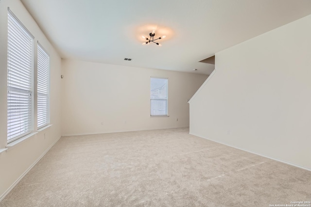 spare room featuring light carpet and an inviting chandelier