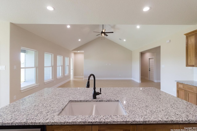 kitchen featuring vaulted ceiling, sink, a kitchen island with sink, and light stone counters