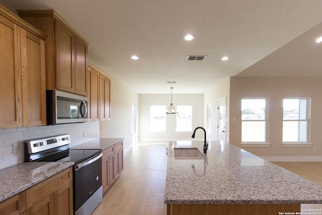 kitchen featuring pendant lighting, sink, appliances with stainless steel finishes, backsplash, and a center island with sink