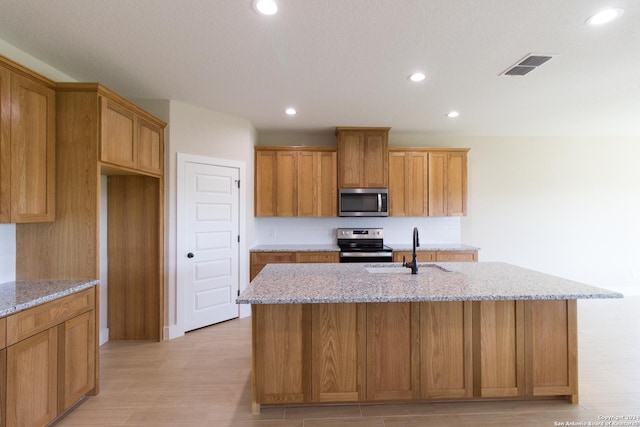 kitchen with sink, light stone countertops, an island with sink, and appliances with stainless steel finishes