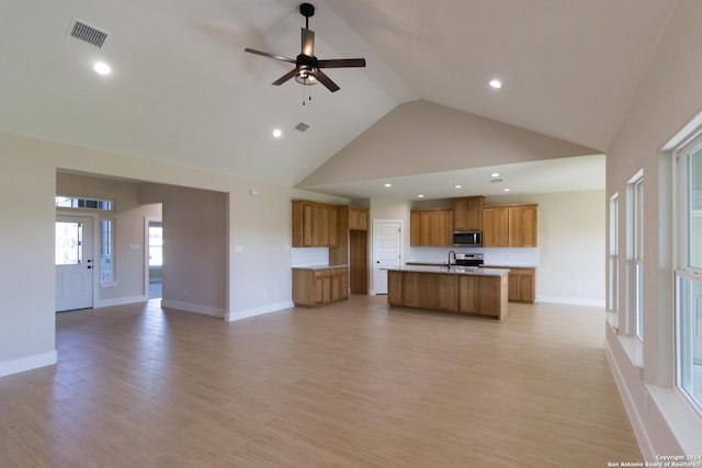 kitchen featuring high vaulted ceiling, sink, an island with sink, and light hardwood / wood-style flooring