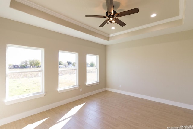 empty room with a raised ceiling, ornamental molding, ceiling fan, and light wood-type flooring