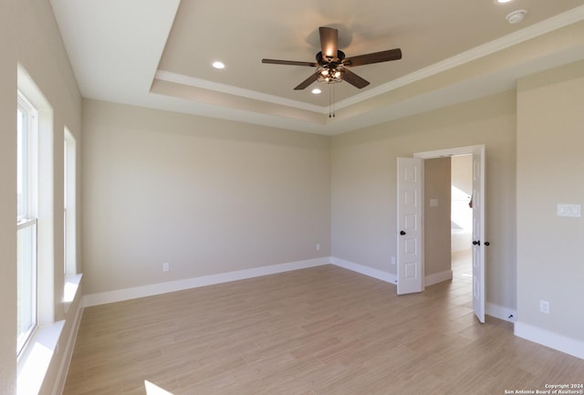 spare room featuring a tray ceiling, ornamental molding, light hardwood / wood-style floors, and ceiling fan