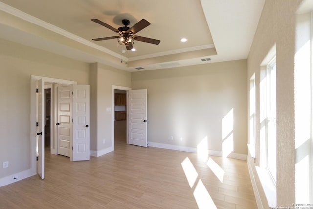 spare room with crown molding, a tray ceiling, ceiling fan, and light wood-type flooring