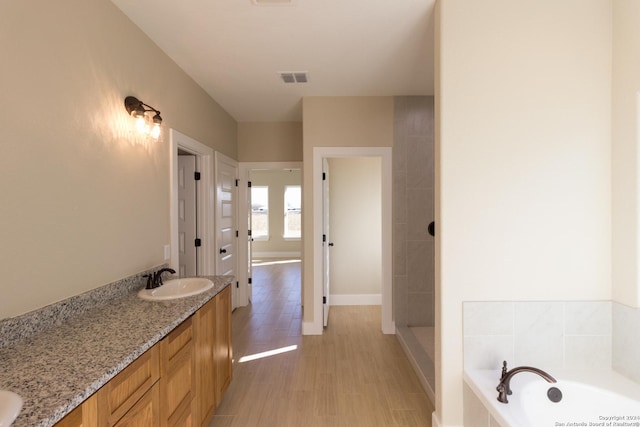 bathroom with a relaxing tiled tub, hardwood / wood-style floors, and vanity