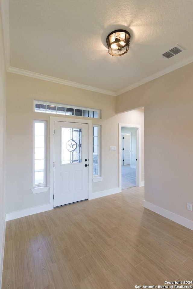 foyer entrance with ornamental molding, a textured ceiling, and light wood-type flooring