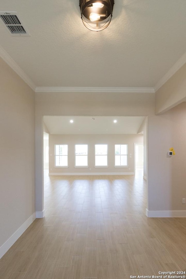 spare room with crown molding, a textured ceiling, and light wood-type flooring