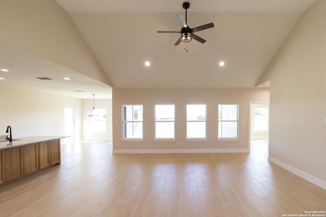 unfurnished living room featuring sink, ceiling fan with notable chandelier, light hardwood / wood-style flooring, and high vaulted ceiling