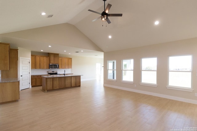 kitchen with light hardwood / wood-style flooring, ceiling fan, appliances with stainless steel finishes, a kitchen island with sink, and high vaulted ceiling