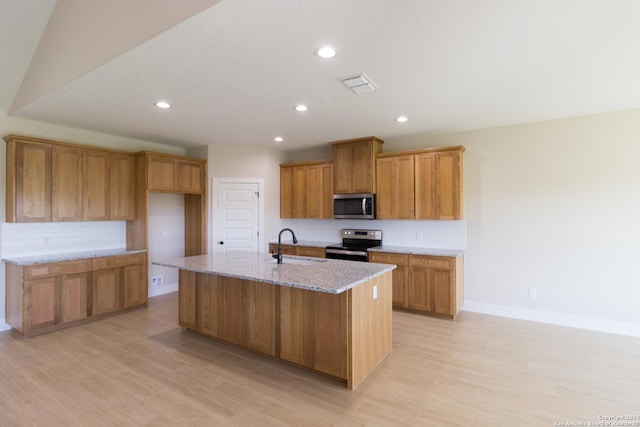 kitchen with sink, light wood-type flooring, an island with sink, stainless steel appliances, and light stone countertops