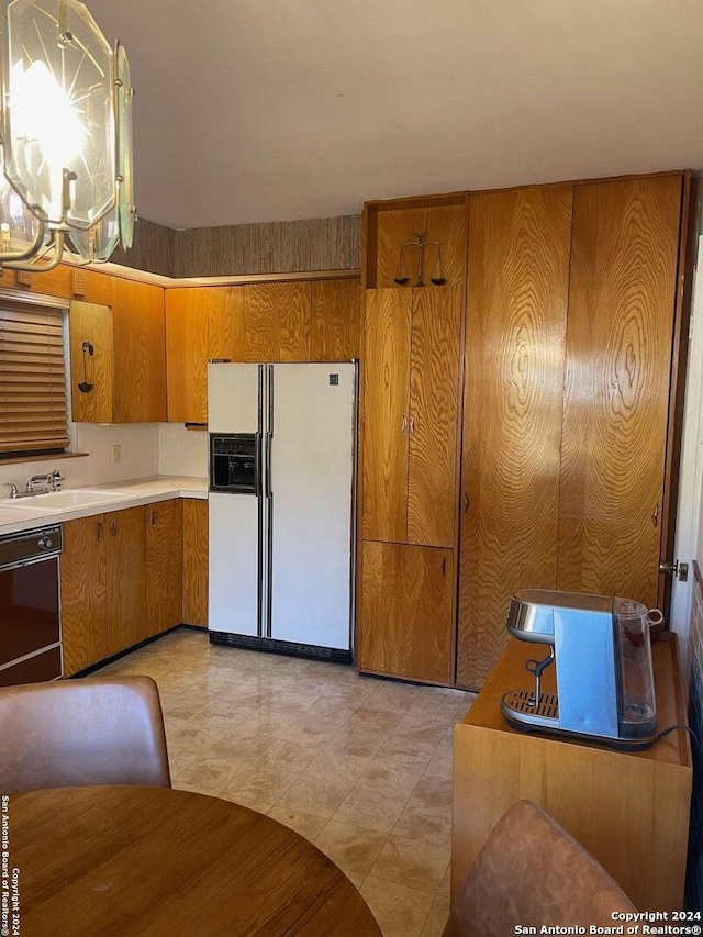 kitchen featuring dishwasher, white fridge with ice dispenser, wooden walls, and sink