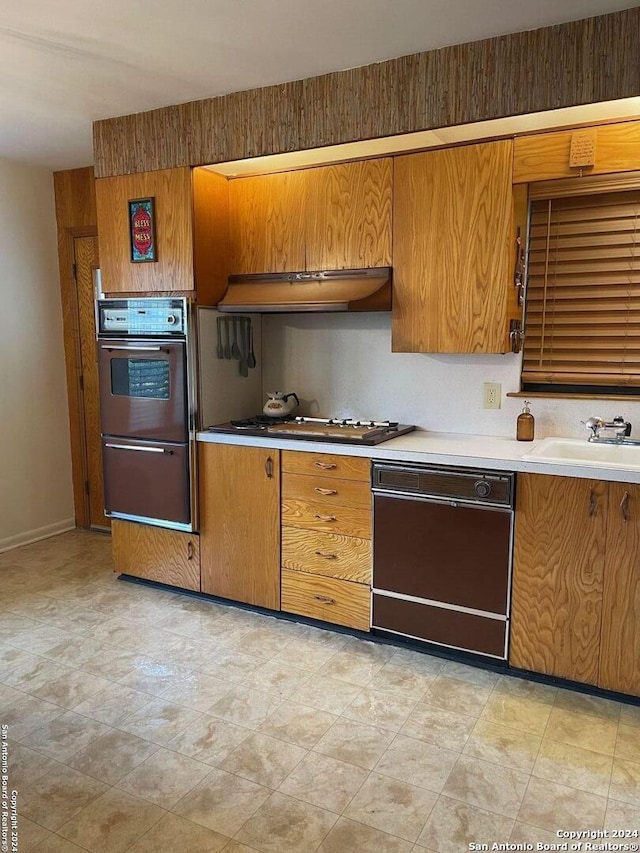 kitchen with double wall oven, premium range hood, stainless steel gas cooktop, sink, and black dishwasher