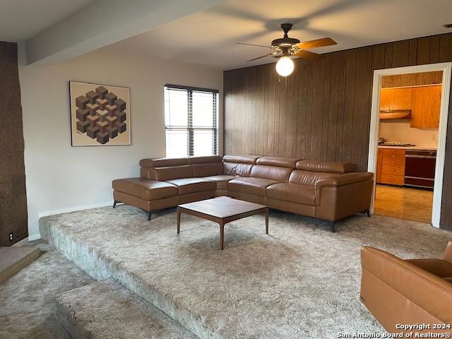 carpeted living room with wooden walls and ceiling fan