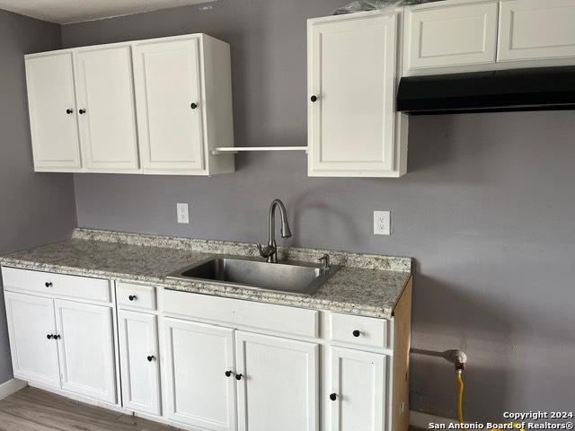 kitchen with white cabinetry, sink, light stone countertops, and wood-type flooring