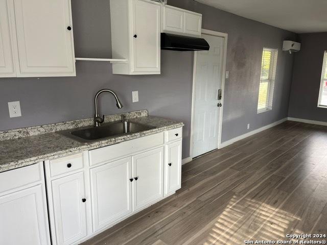 kitchen featuring light stone counters, ventilation hood, dark wood-type flooring, sink, and white cabinetry